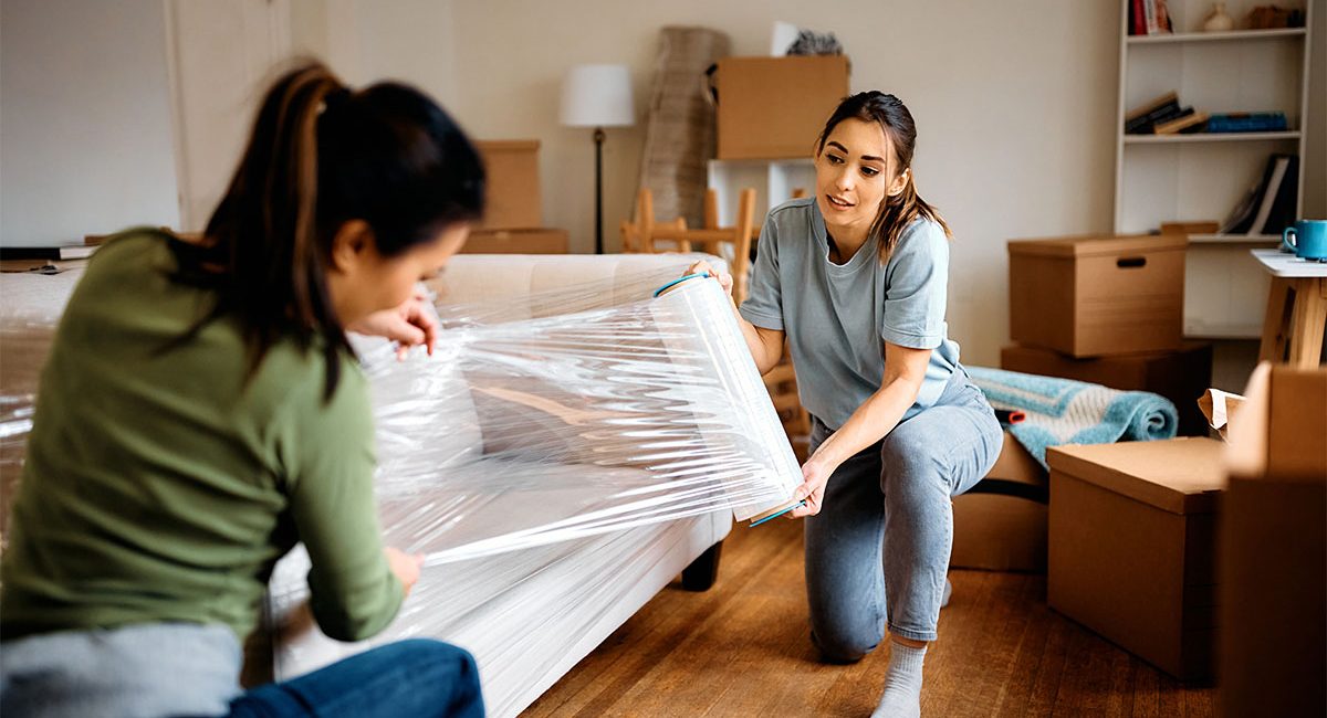 Young women wrapping furniture on their moving day.