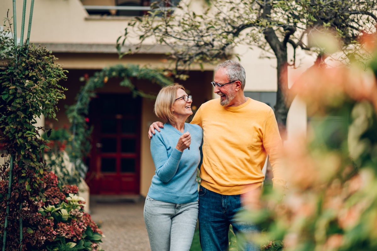 Senior couple holding keys and standing outside their new home