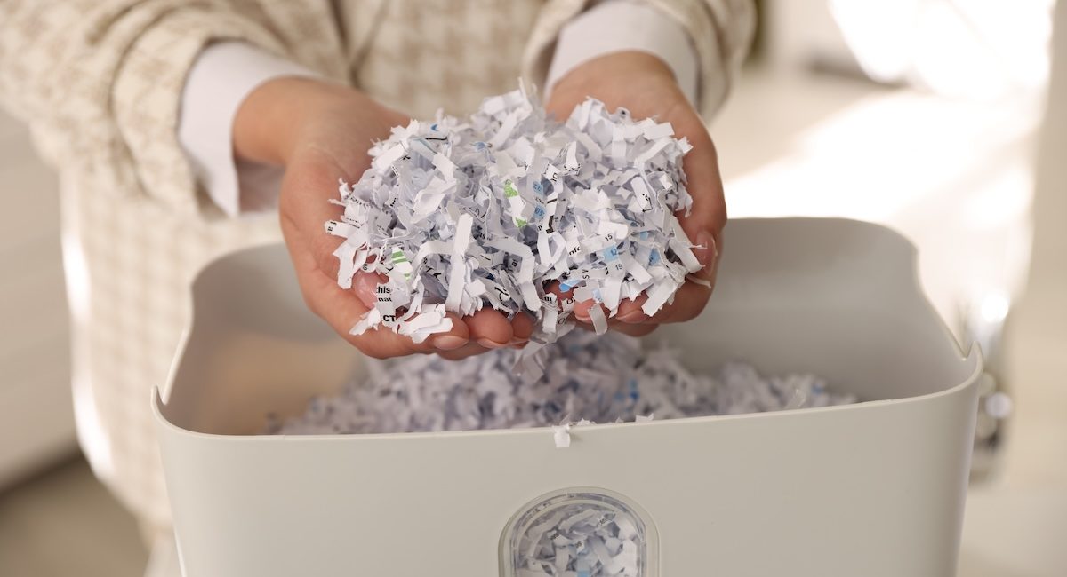 Woman taking out cut paper pieces from shredder bin in office